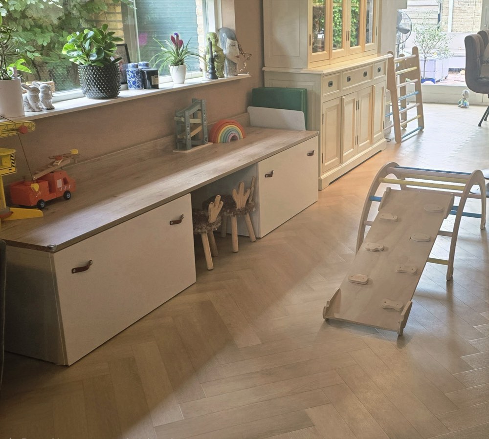 Huiselijke speelruimte met houten speelgoed en een klimdriehoek.